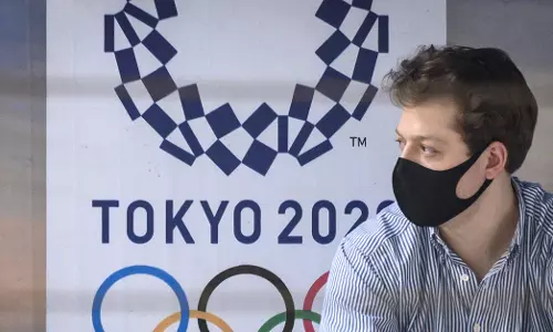 A man wearing a face mask sits at a bus stop in front of a Tokyo 2020 Olympics advertisement in March, 2020. (Source: Mladen Antonov / Getty)