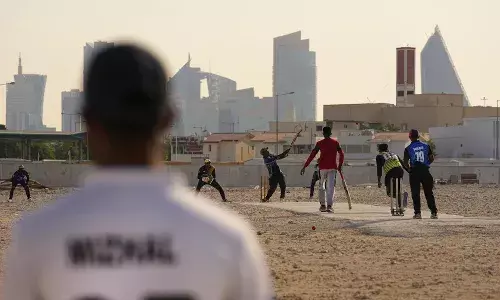 Laborers play sandlot cricket near World Cup football stadiums