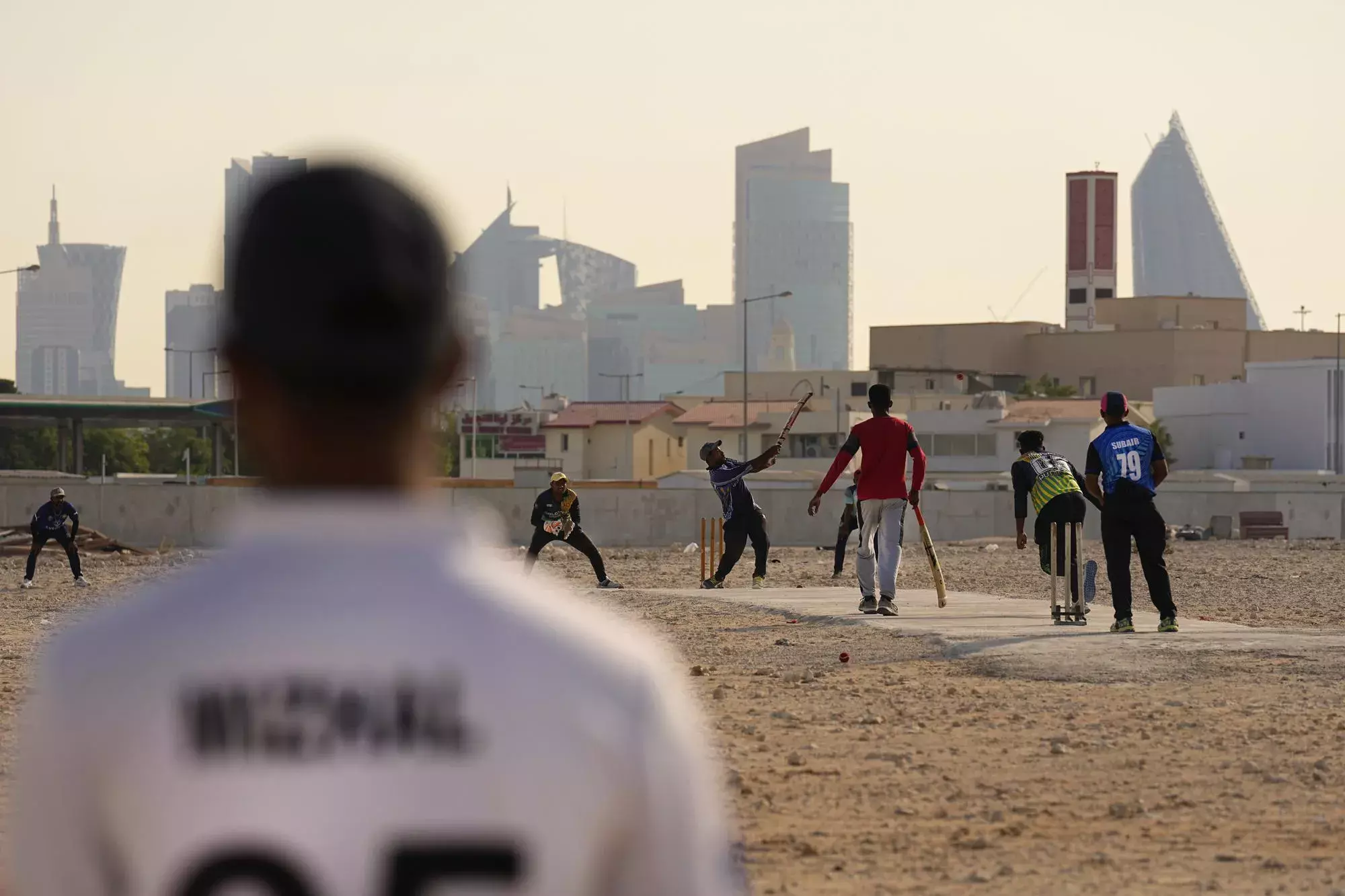 Laborers play sandlot cricket near World Cup football stadiums